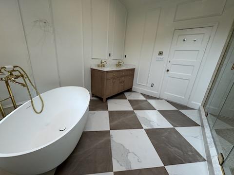 Modern bathroom with a freestanding white bathtub, brown and white checkered floor tiles, wooden vanity with two sinks, and a glass shower enclosure.