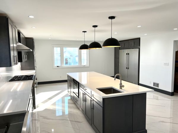 Modern kitchen with large island, black cabinetry, white countertops, black pendant lights, and stainless steel appliances.