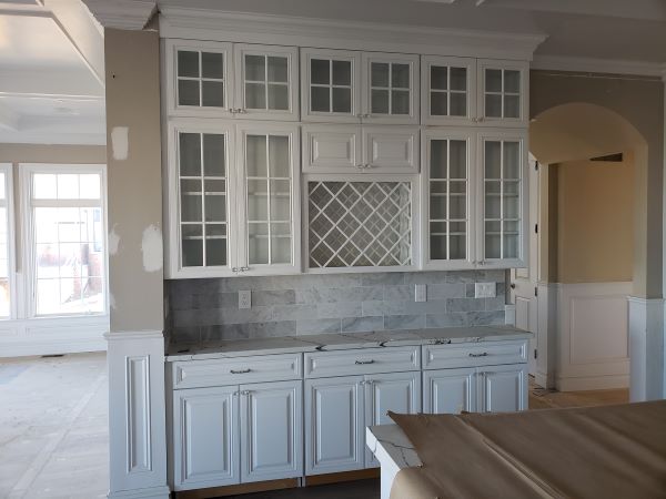 White kitchen cabinets with glass-paneled doors and a wine rack, set against a gray tiled backsplash.