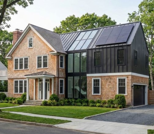 Modern suburban house featuring wood shingle siding, large glass central section, black metal roofing with solar panels, and a well-maintained front lawn.