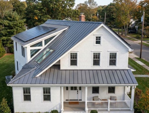 White two-story house with a metal roof featuring solar panels and skylights.