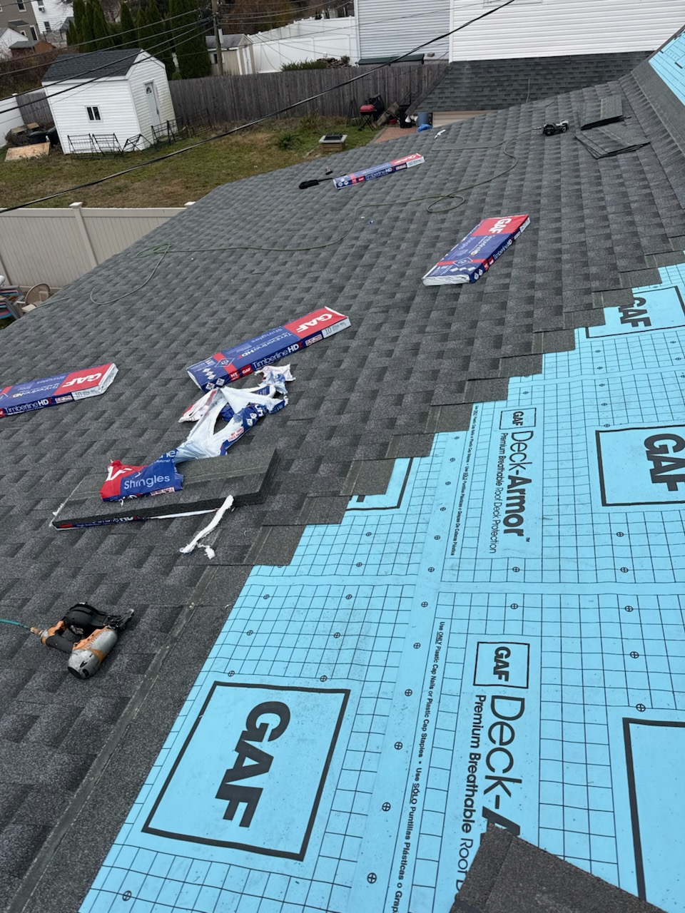 Two-story suburban house with shingle siding, a metal roof featuring solar panels and a skylight, surrounded by greenery and a paved driveway.