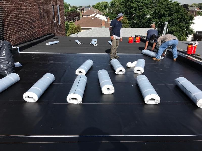 Modern two-story house with wood siding and large glass windows, featuring a black metal roof with solar panels.
