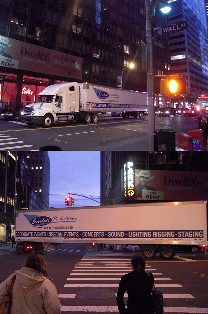 White Everlast Productions truck with trailer parked and crossing a city street at night in New York, near Wall Street with pedestrians waiting at a crosswalk.