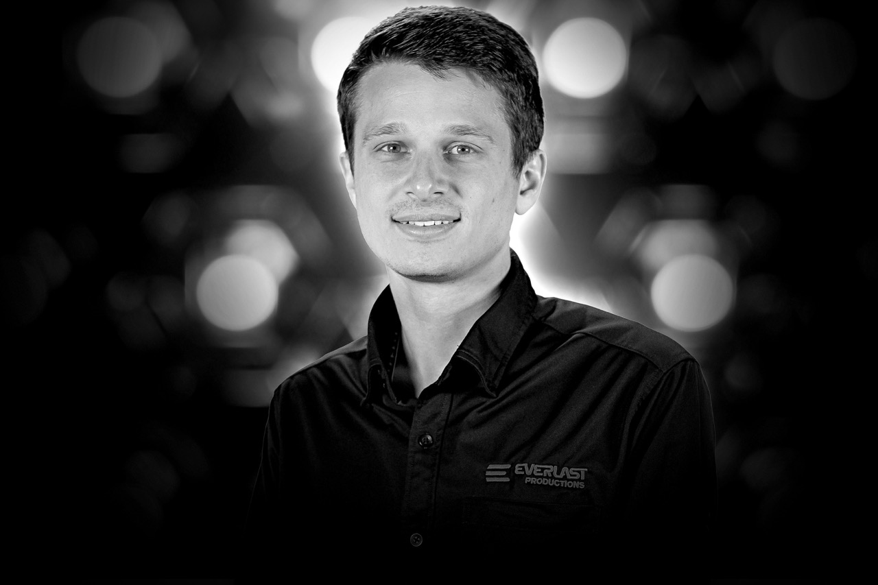 Portrait of a young man wearing a black Everlast Productions shirt with a blurred light bokeh background.