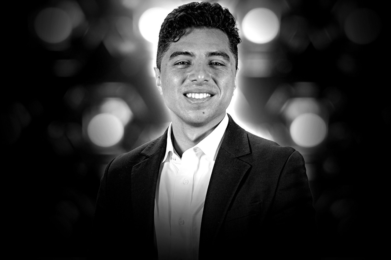 Black and white headshot of a smiling man with short curly hair wearing a dark blazer and white shirt.