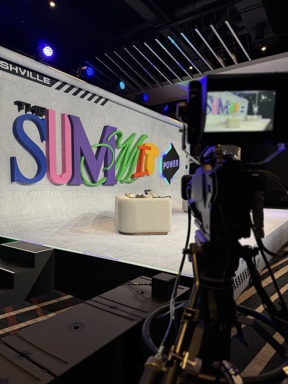 Colorful 3D letters spelling THE SUMMIT POWER on a stage with a camera recording.