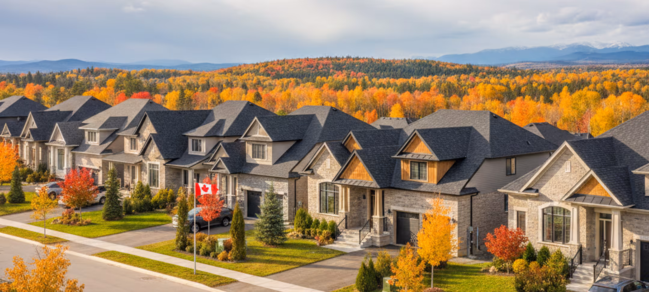 Row of suburban houses with dark roofs and fall foliage in the background, including a Canadian flag on a lawn.