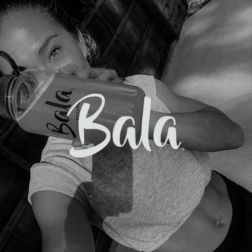 Woman in a cropped t-shirt drinking from a water bottle with Bala logo.