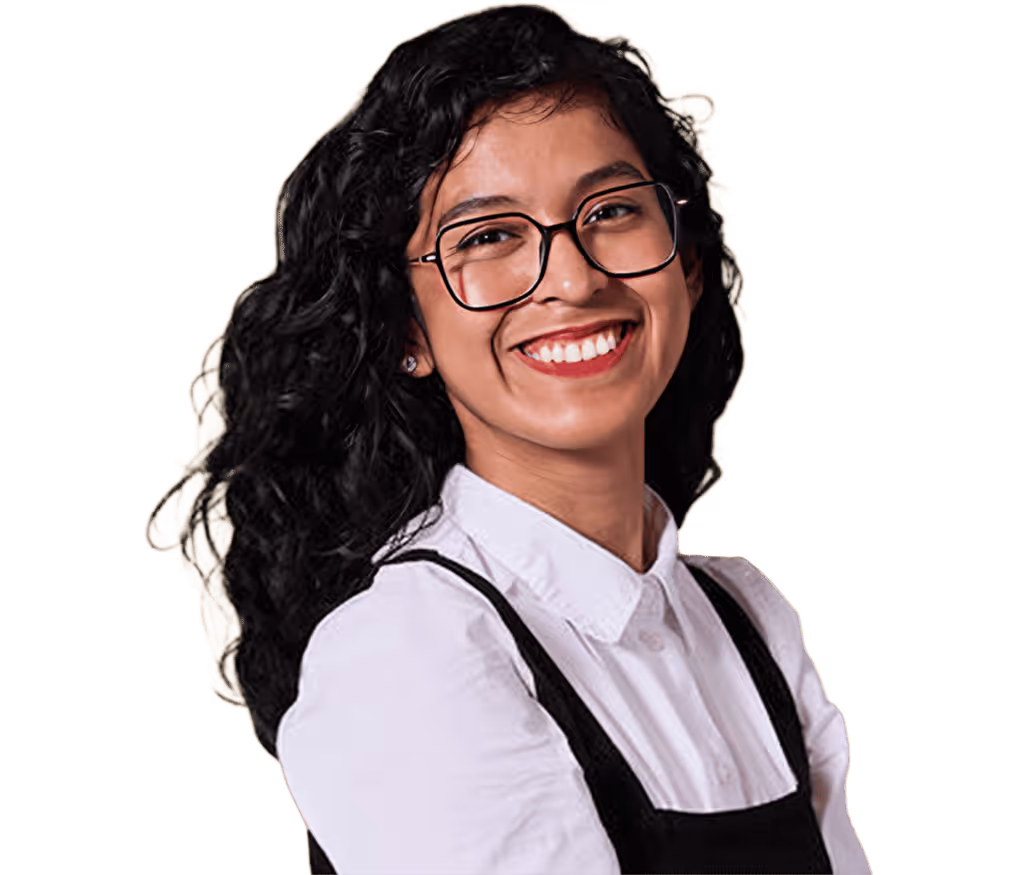 Mujer joven con cabello rizado oscuro, gafas y sonrisa amplia, vestida con camisa blanca y sobrepelliz negra.