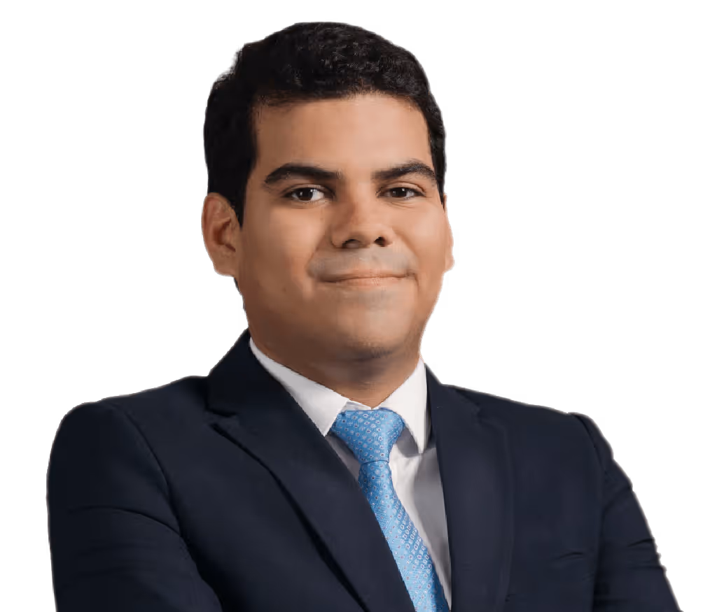Hombre calvo con gafas redondas oscuras, camisa beige y collar de perlas sonriente.
