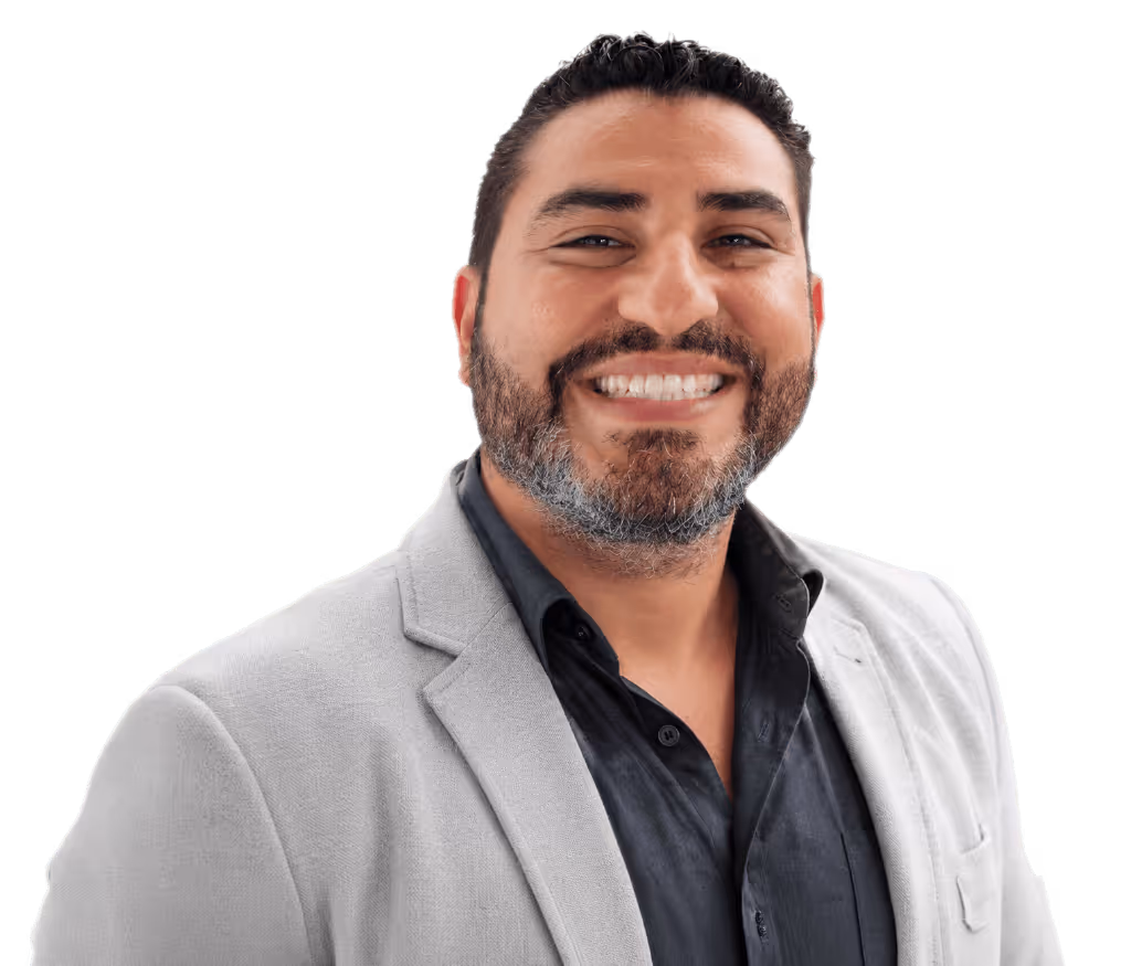 Hombre calvo con gafas redondas oscuras, camisa beige y collar de perlas sonriente.