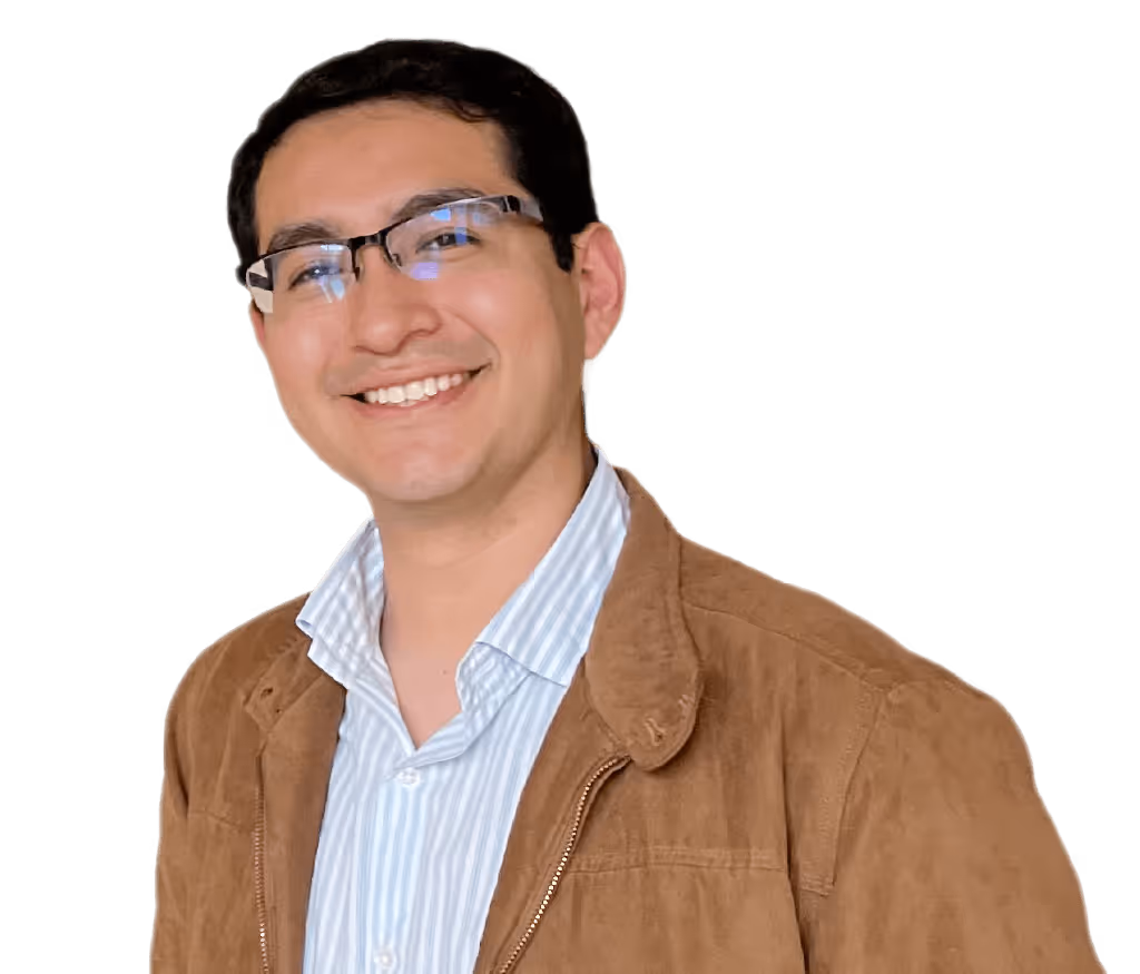 Hombre calvo con gafas redondas oscuras, camisa beige y collar de perlas sonriente.