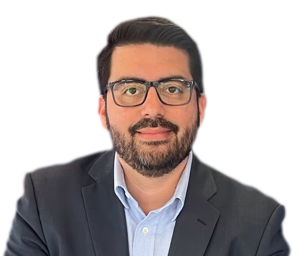 Hombre calvo con gafas redondas oscuras, camisa beige y collar de perlas sonriente.
