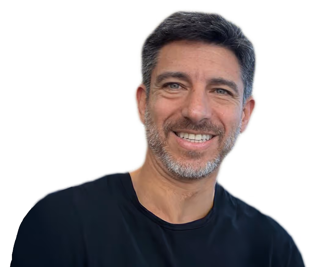 Hombre calvo con gafas redondas oscuras, camisa beige y collar de perlas sonriente.