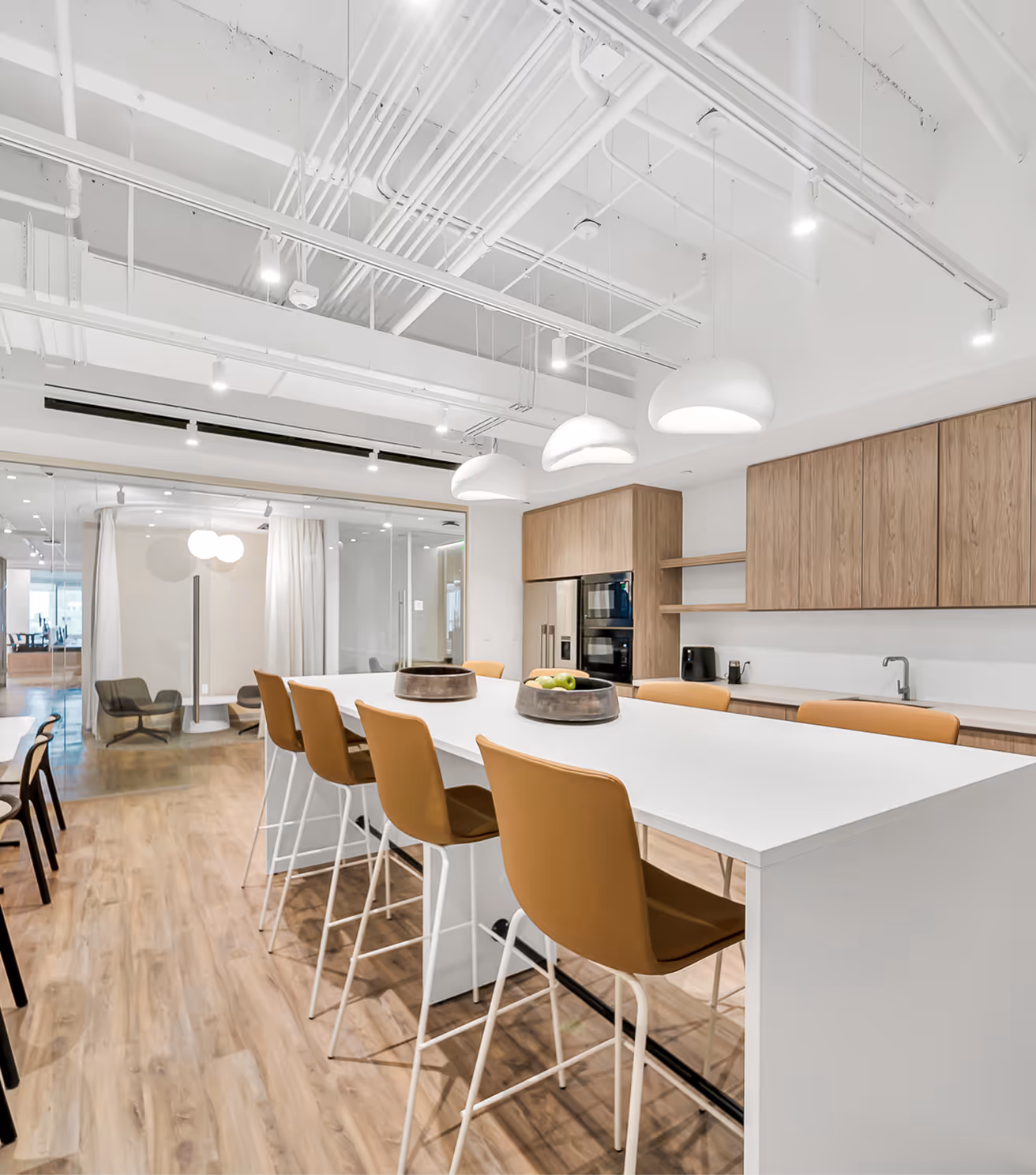 Modern office kitchen with white island, five brown bar stools, wooden cabinets, and pendant lights.