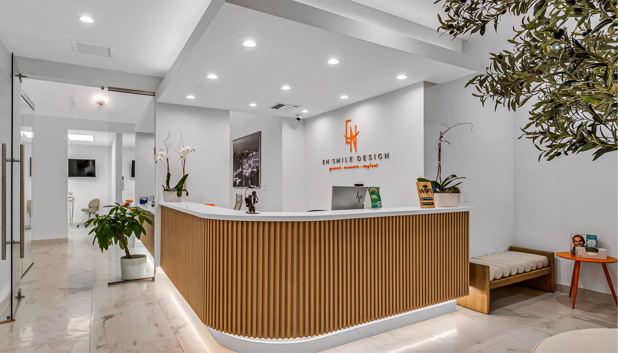 Modern dental office reception area with a wooden slat front desk, white countertop, plants, and signage reading EN Smile Design.
