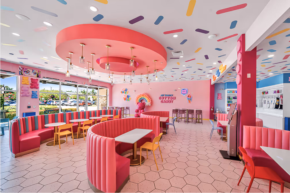 Brightly colored, modern ice cream shop interior with pink curved booths, yellow and red chairs, and playful wall and ceiling decorations.