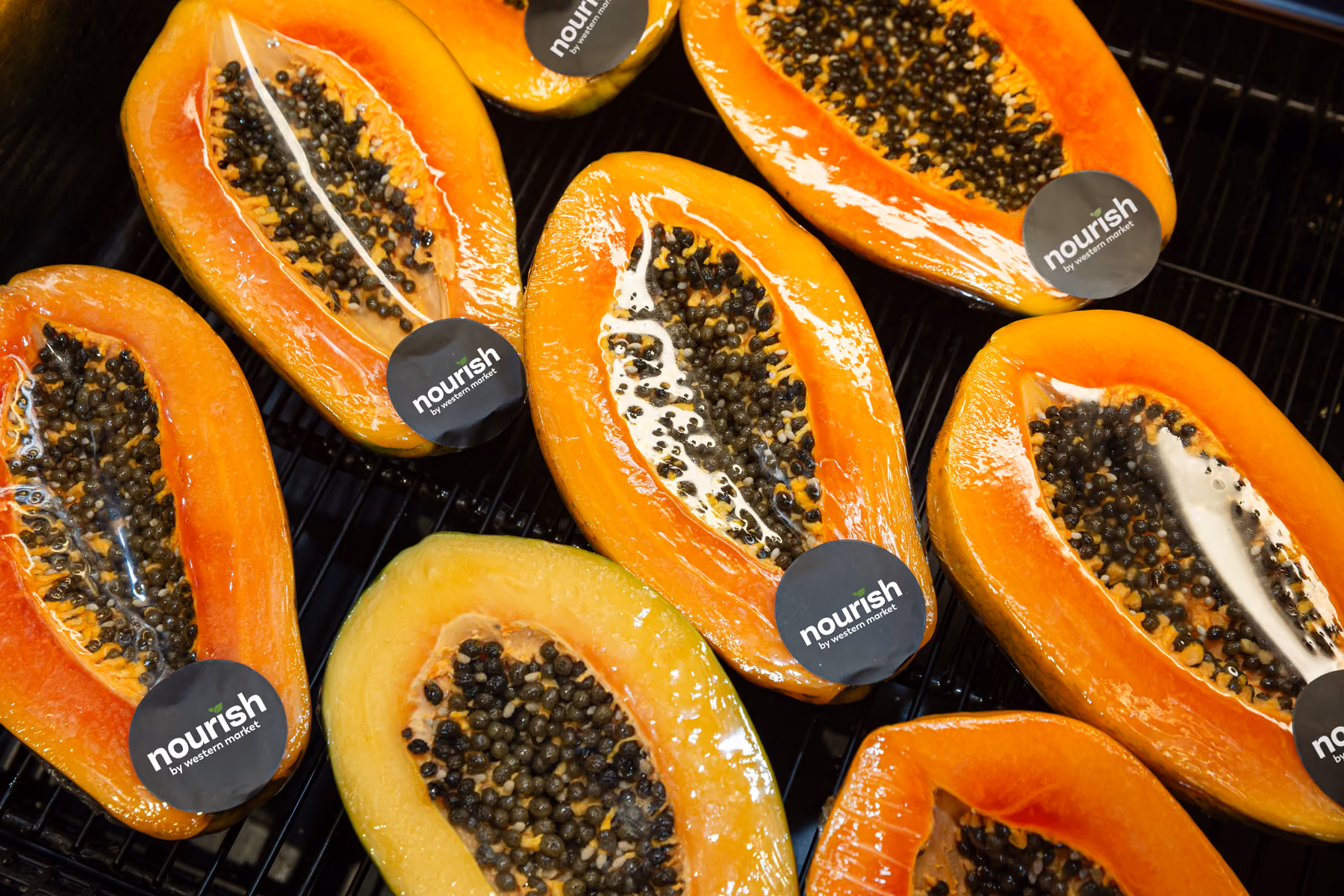 Halved papayas with seeds and nourish by western market stickers on a black surface.