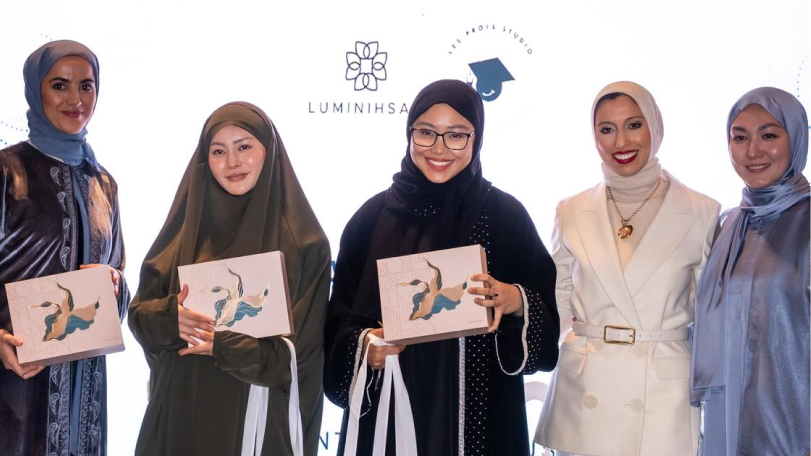 Five women wearing hijabs standing in a row, three holding award boxes and smiling at the camera.