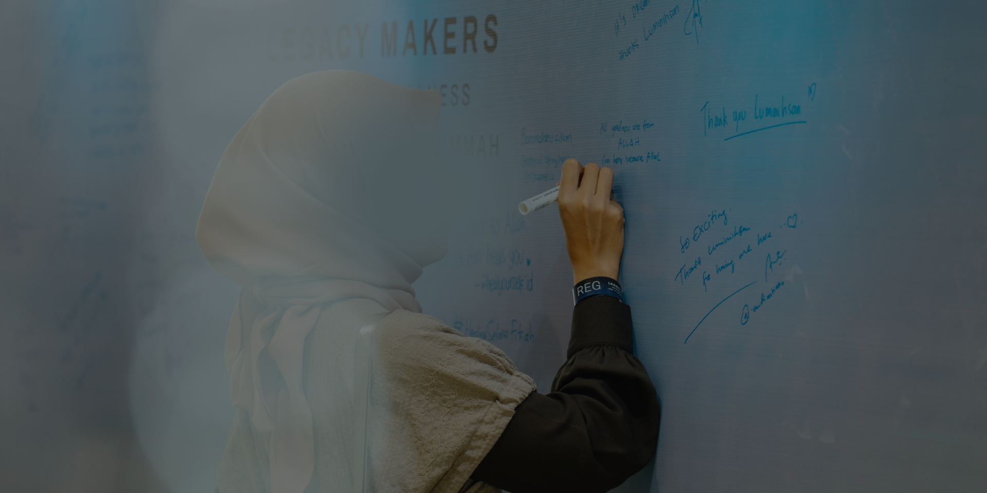 Person wearing a white headscarf writing messages with a blue marker on a whiteboard wall filled with handwritten notes.