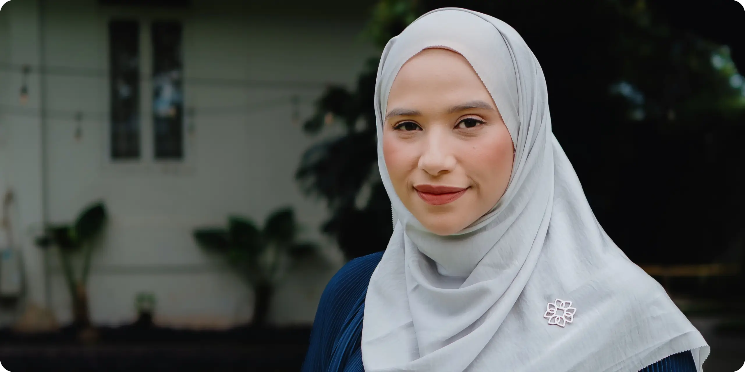 Woman in white hijab looking emotional among other women in headscarves in a dimly lit setting.