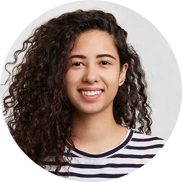 Smiling young woman with curly dark hair wearing a black and white striped shirt against a light background.