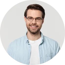 Smiling man with glasses, wearing a light blue shirt over a white t-shirt, against a plain background.