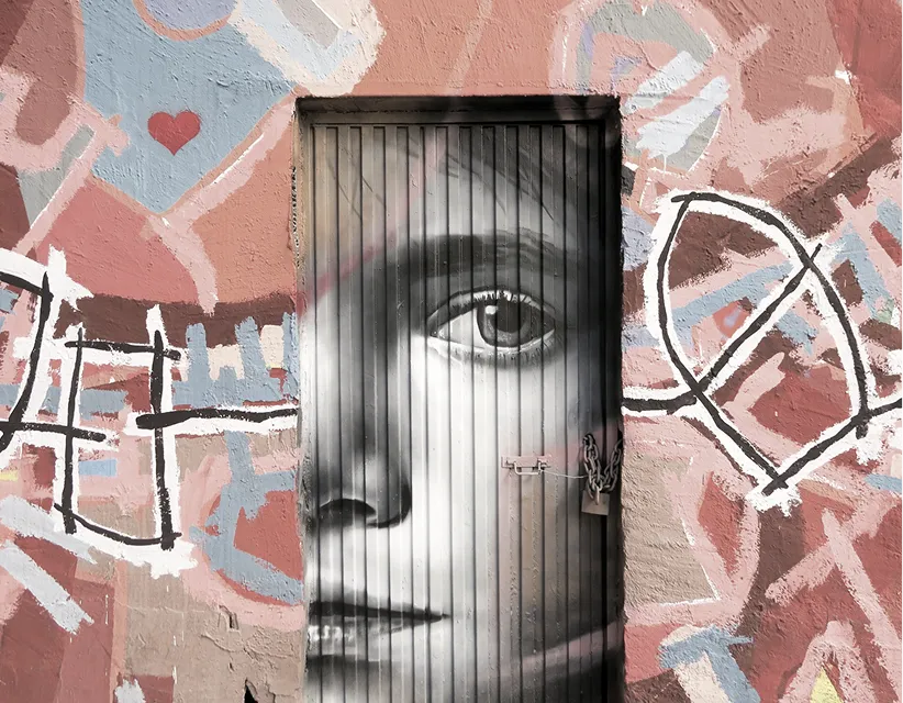 Black and white mural of a woman's face painted on a closed door set in a pink wall with abstract graffiti.