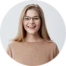 Smiling young woman with long light brown hair, wearing glasses and a beige sweater, against a white background.