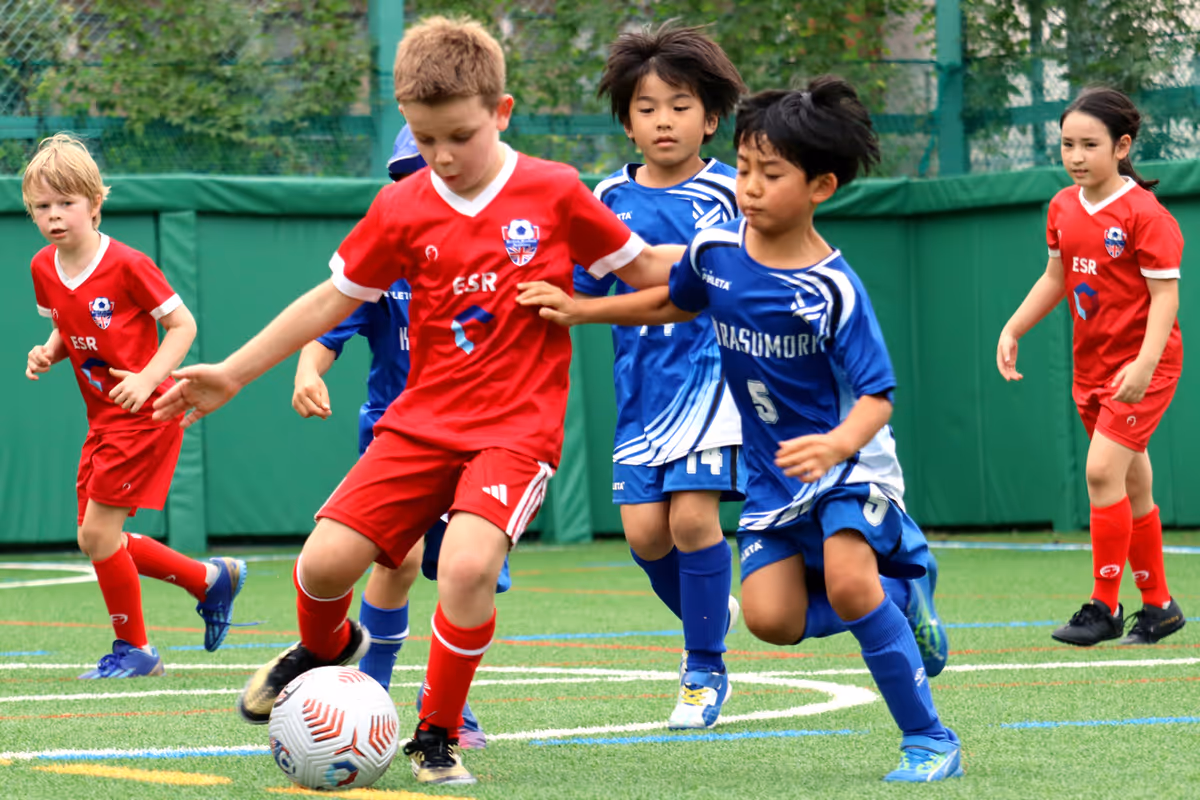 Children playing soccer on a green field with some wearing red uniforms and others in blue.