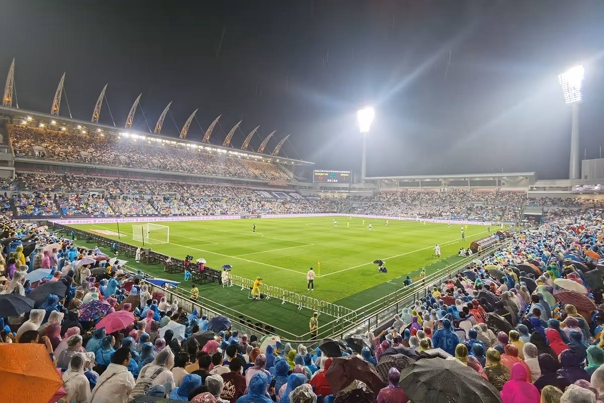 Children playing soccer on a green field with one boy in a red jersey dribbling the ball while a boy in blue tries to block him.