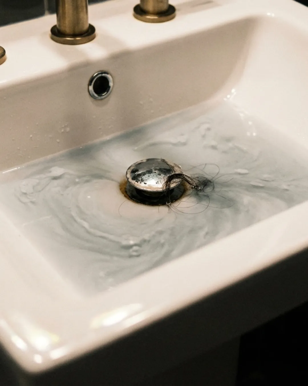 Bathroom basin with slow-draining murky water and brass fixtures in a Balmain terrace
