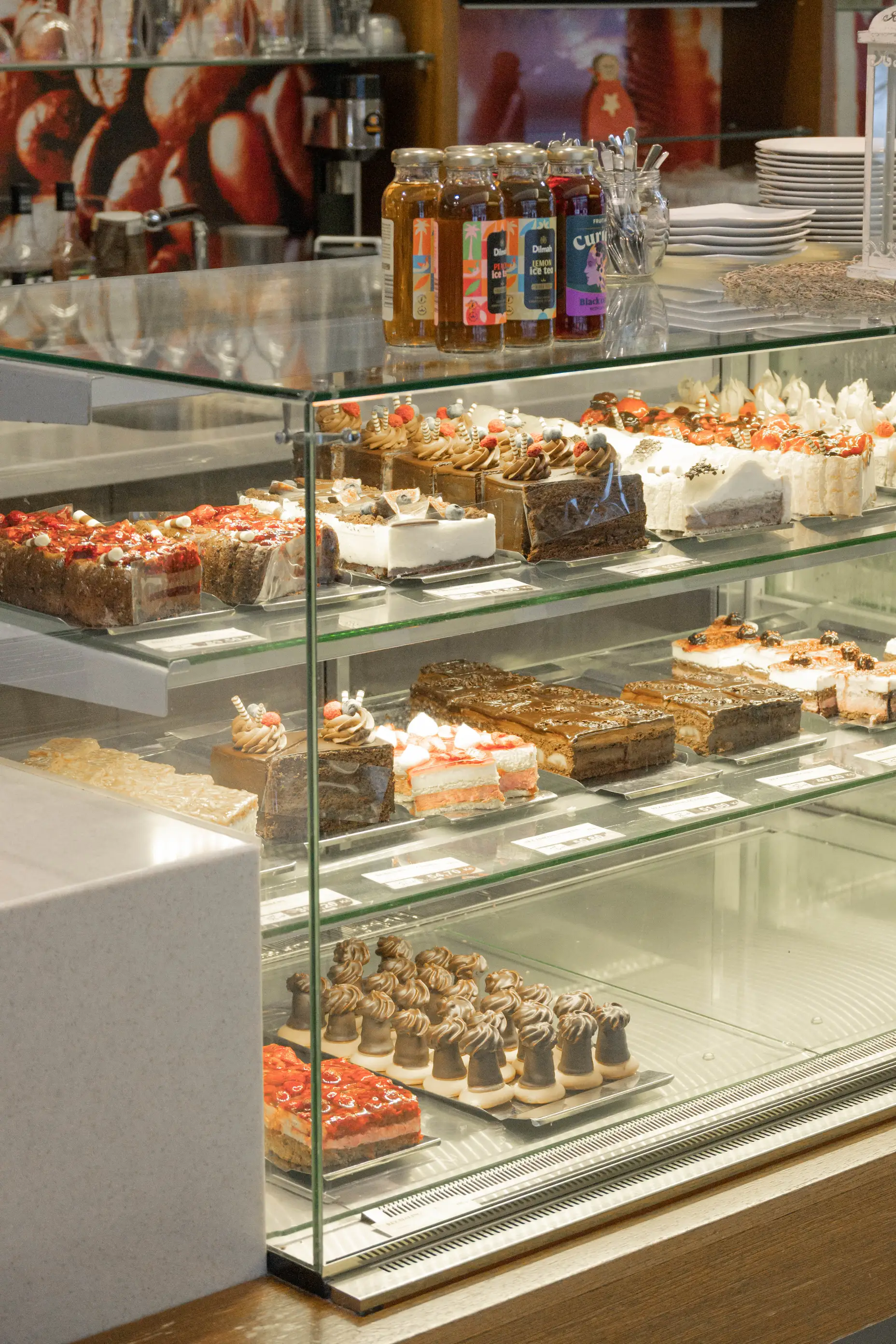Skleněná vitrína v cukrárně s různými druhy dortů a dezertů na několika policích.