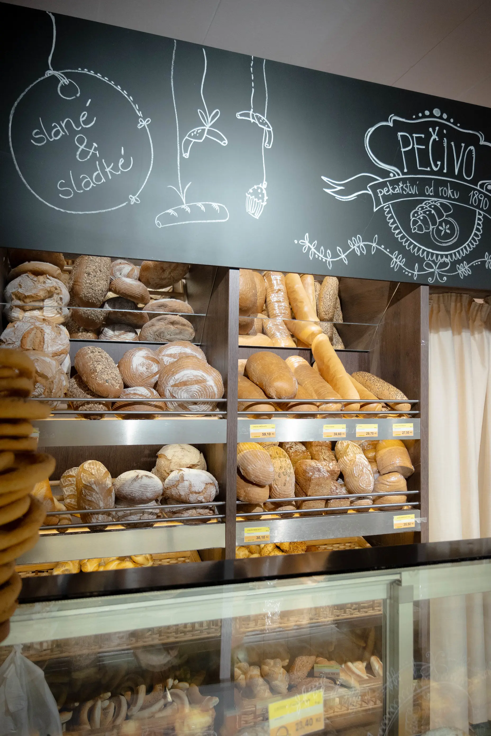 Pekařství s regály plnými různých druhů čerstvého pečiva a nápisem slané a sladké na tabuli nad nimi.