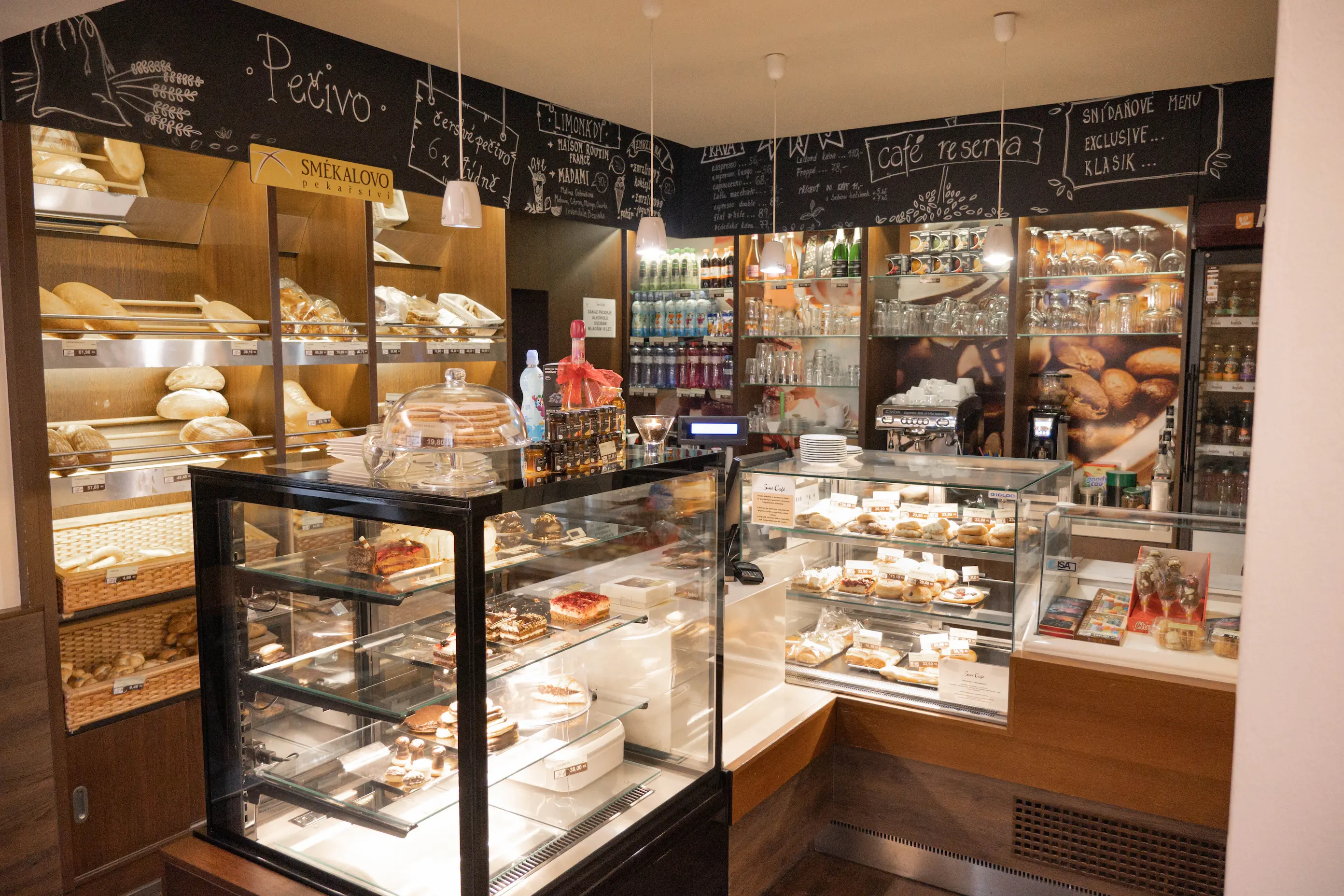 Interiér pekárny s vitrínami plnými pečiva, dezertů a kavovarem na pozadí.