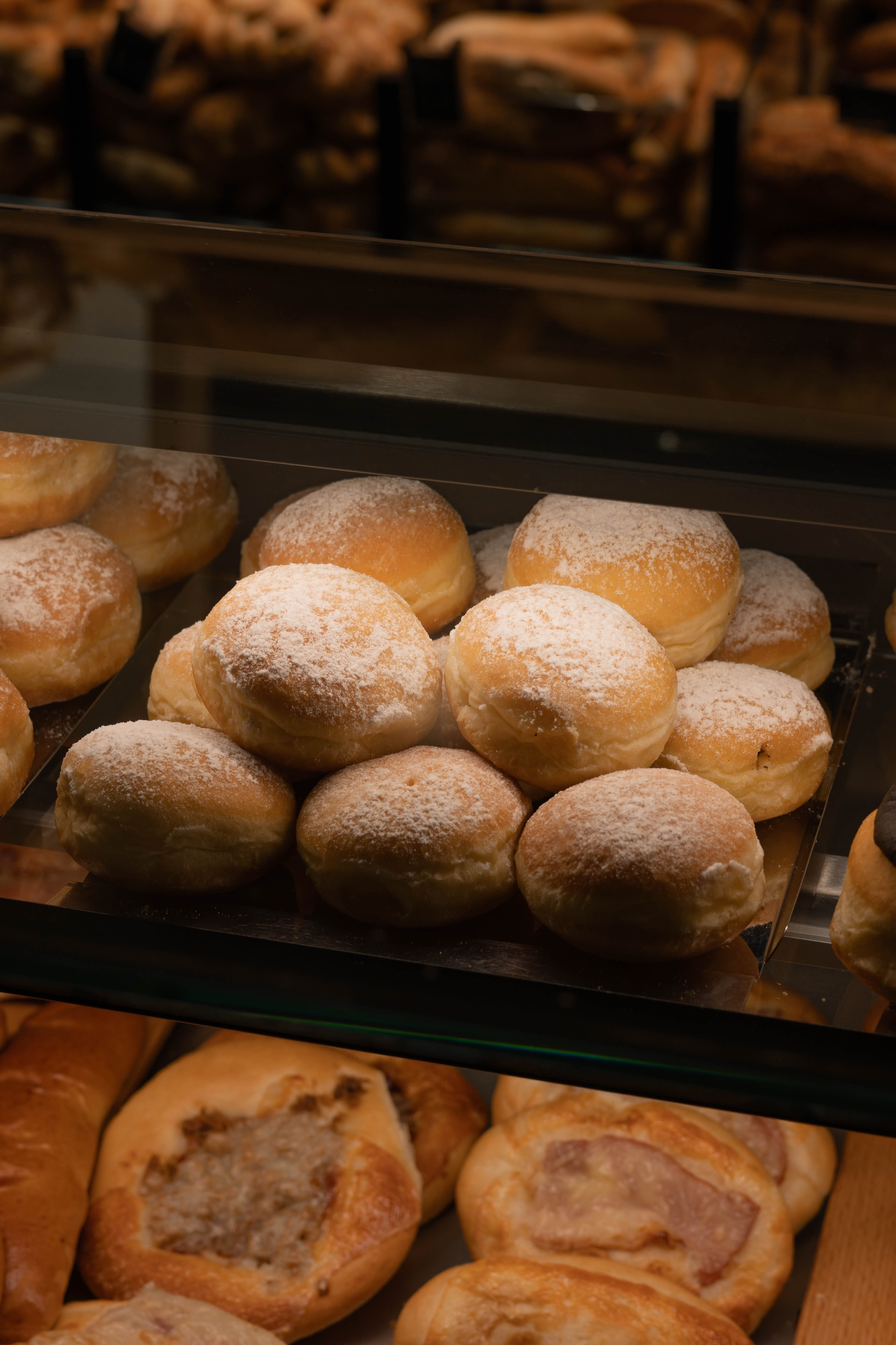 Plech s koblížky posypanými moučkovým cukrem v cukrárně.