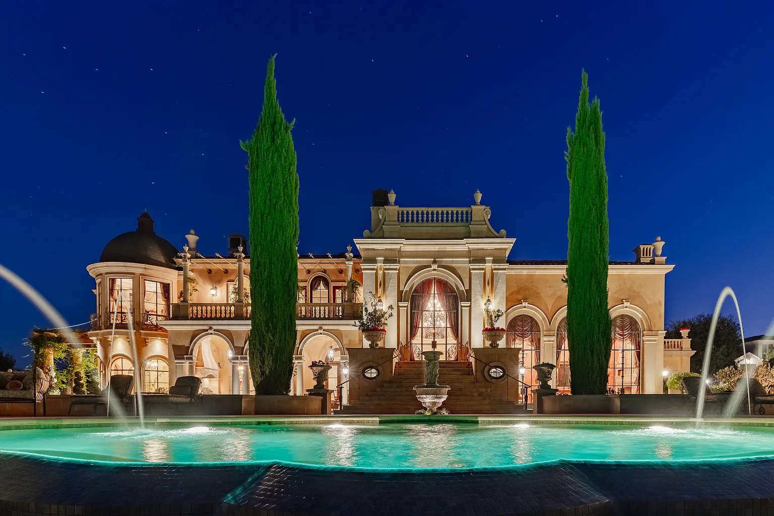 Night exterior view of a $17 million Italianate luxury mansion in Calabasas featuring illuminated façade, grand staircase, and resort-style swimming pool with fountains