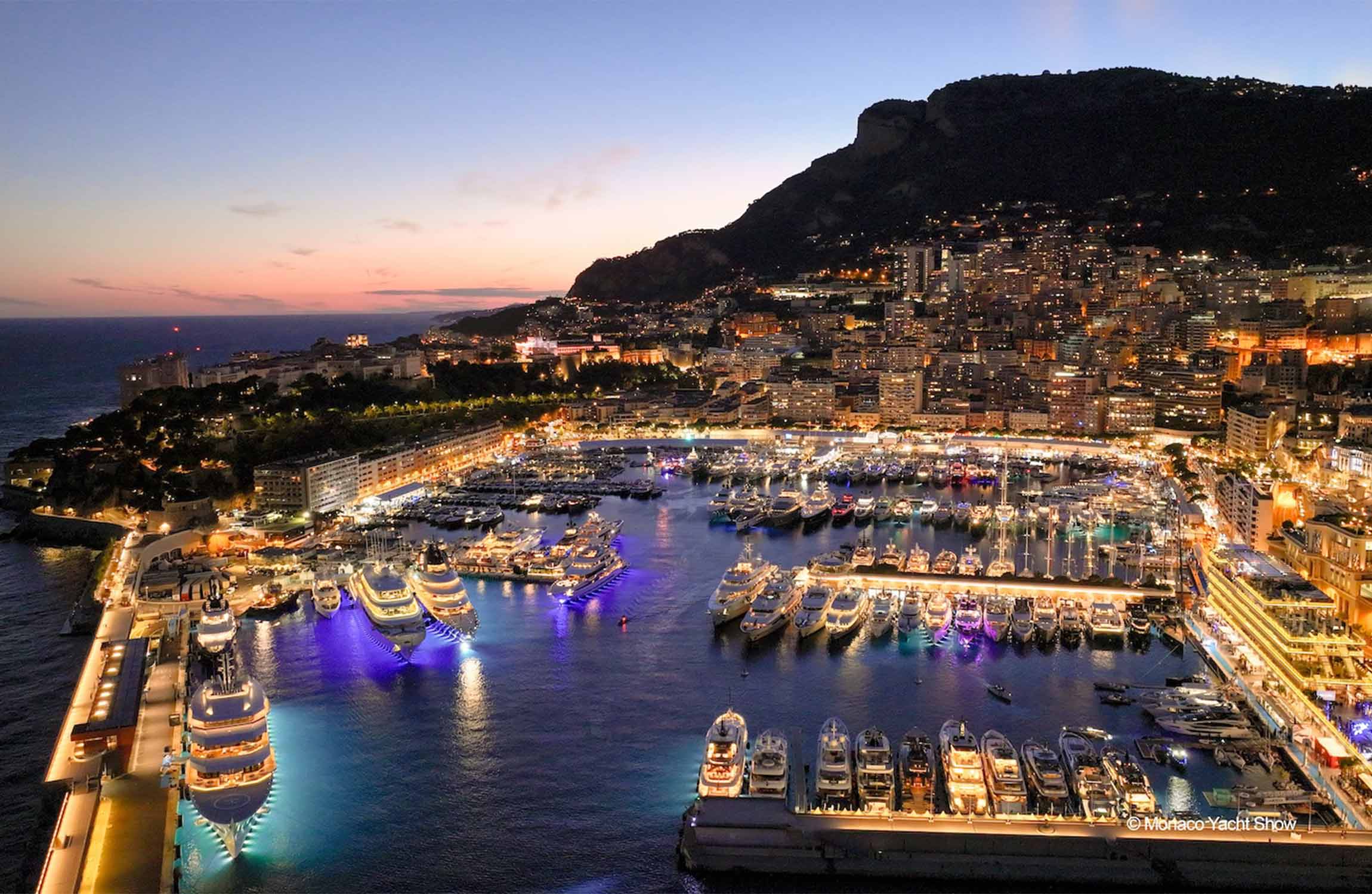 Aerial night view of Port Hercule Monaco filled with luxury superyachts and illuminated Mediterranean skyline during the Monaco Yacht Show atmosphere
