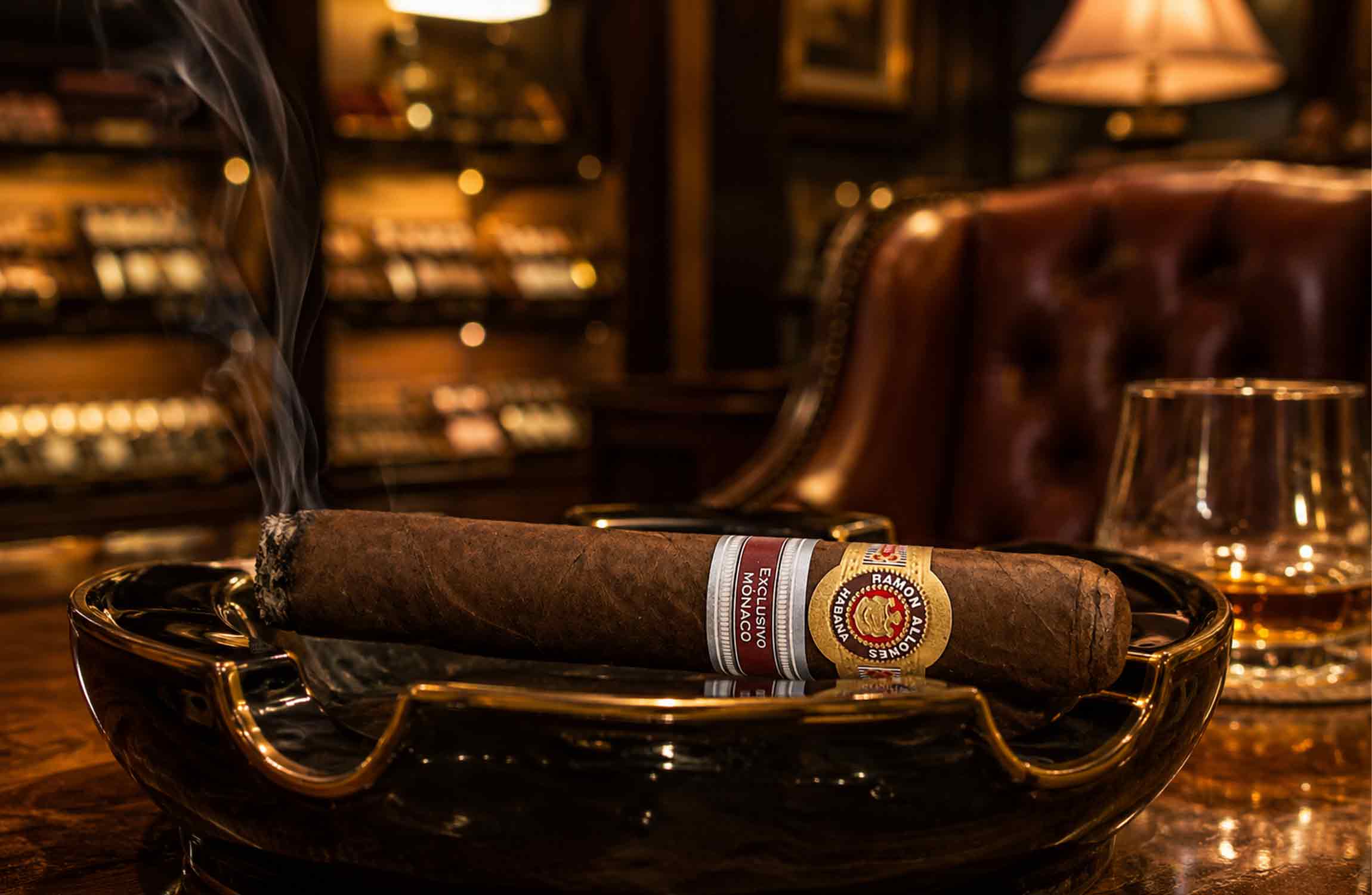 Ramon Allones Exclusivo Monaco cigar resting in a luxury ashtray inside an elegant cigar lounge, surrounded by warm ambient lighting, aged spirits, and refined club atmosphere.