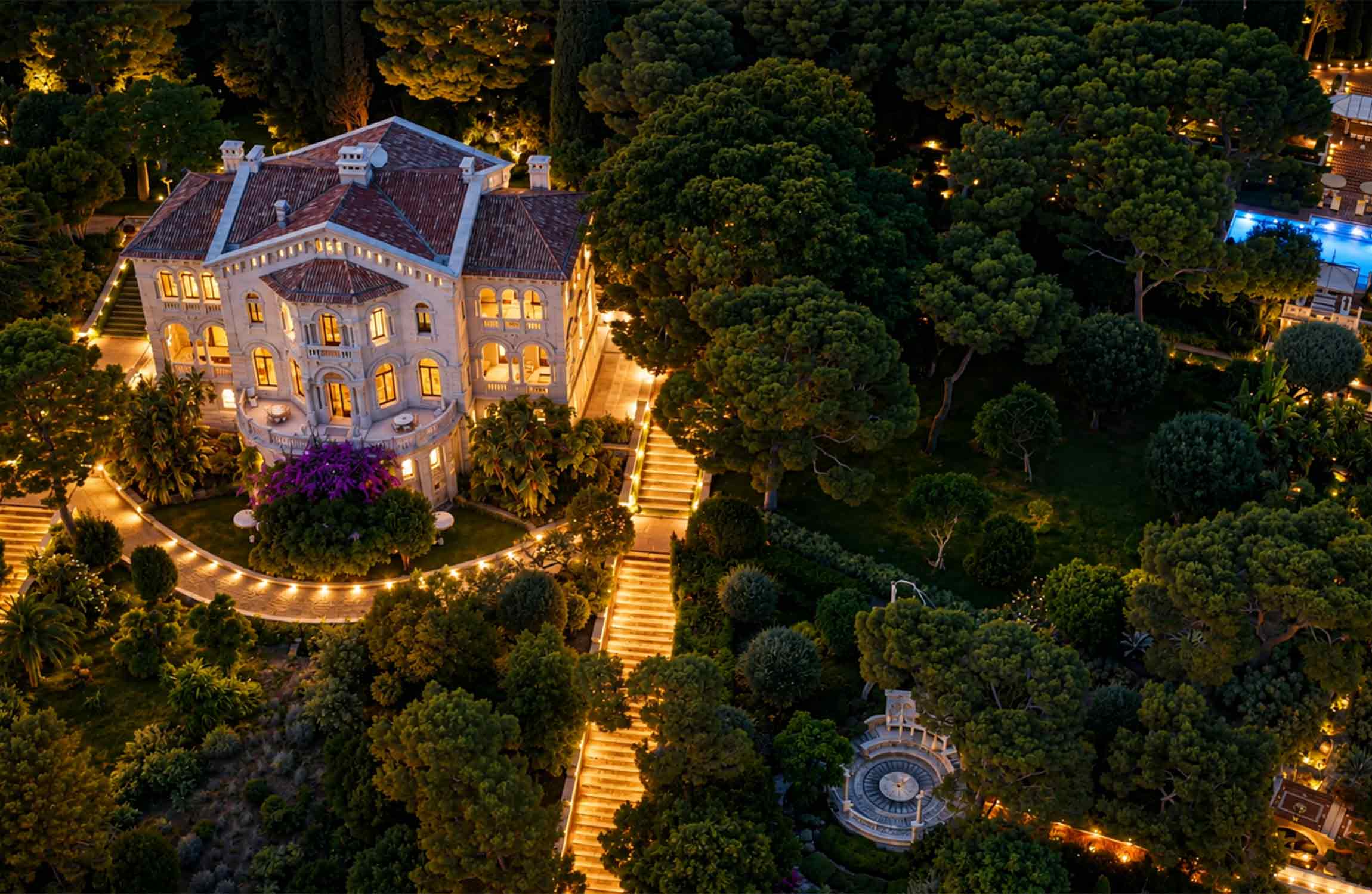 Aerial night view of Villa Cypris in Roquebrune-Cap-Martin, surrounded by illuminated Mediterranean gardens near Monaco on the French Riviera.