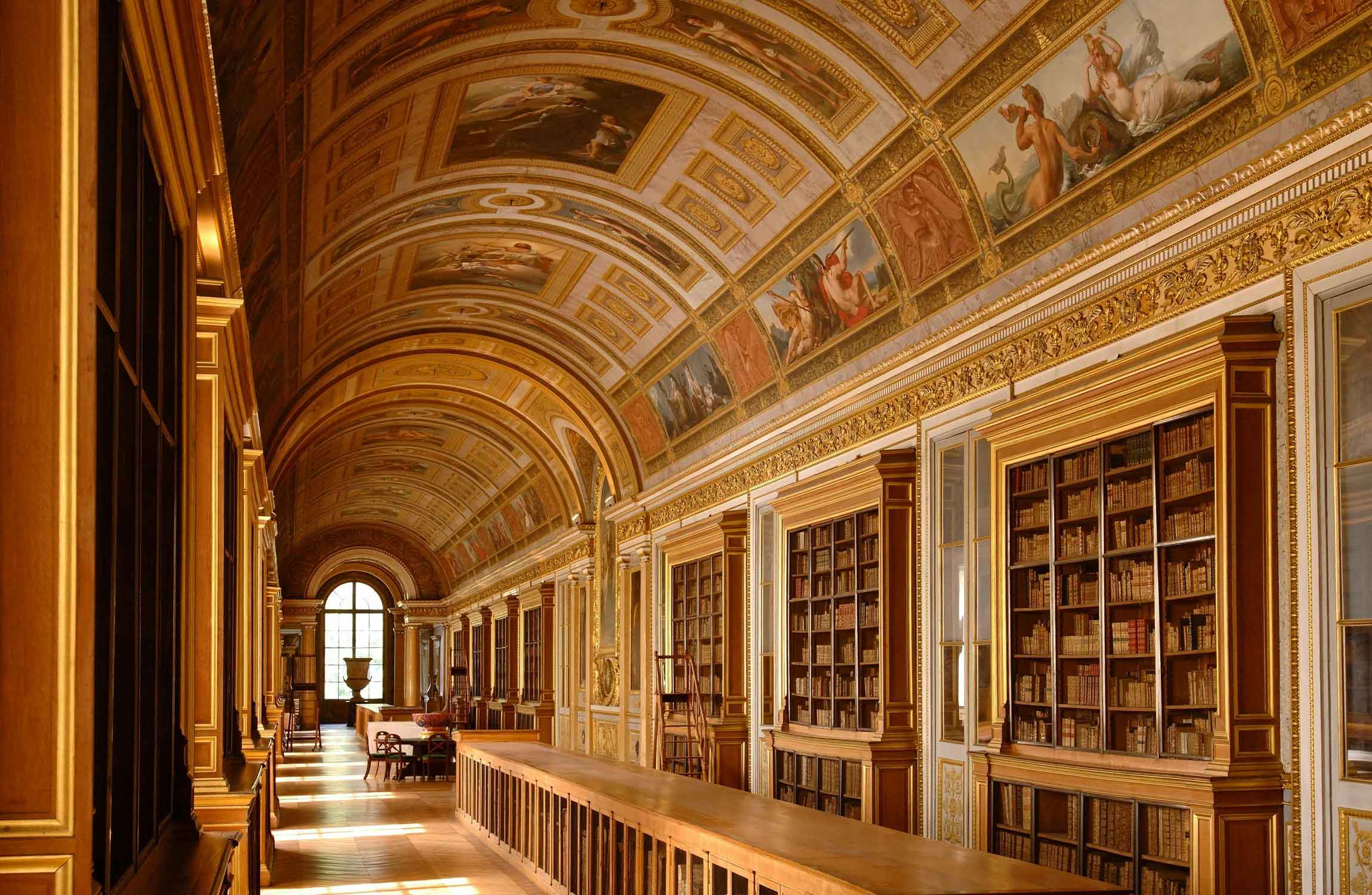 Historic library at the Château de Fontainebleau with rare books, gilded details and a painted vaulted ceiling