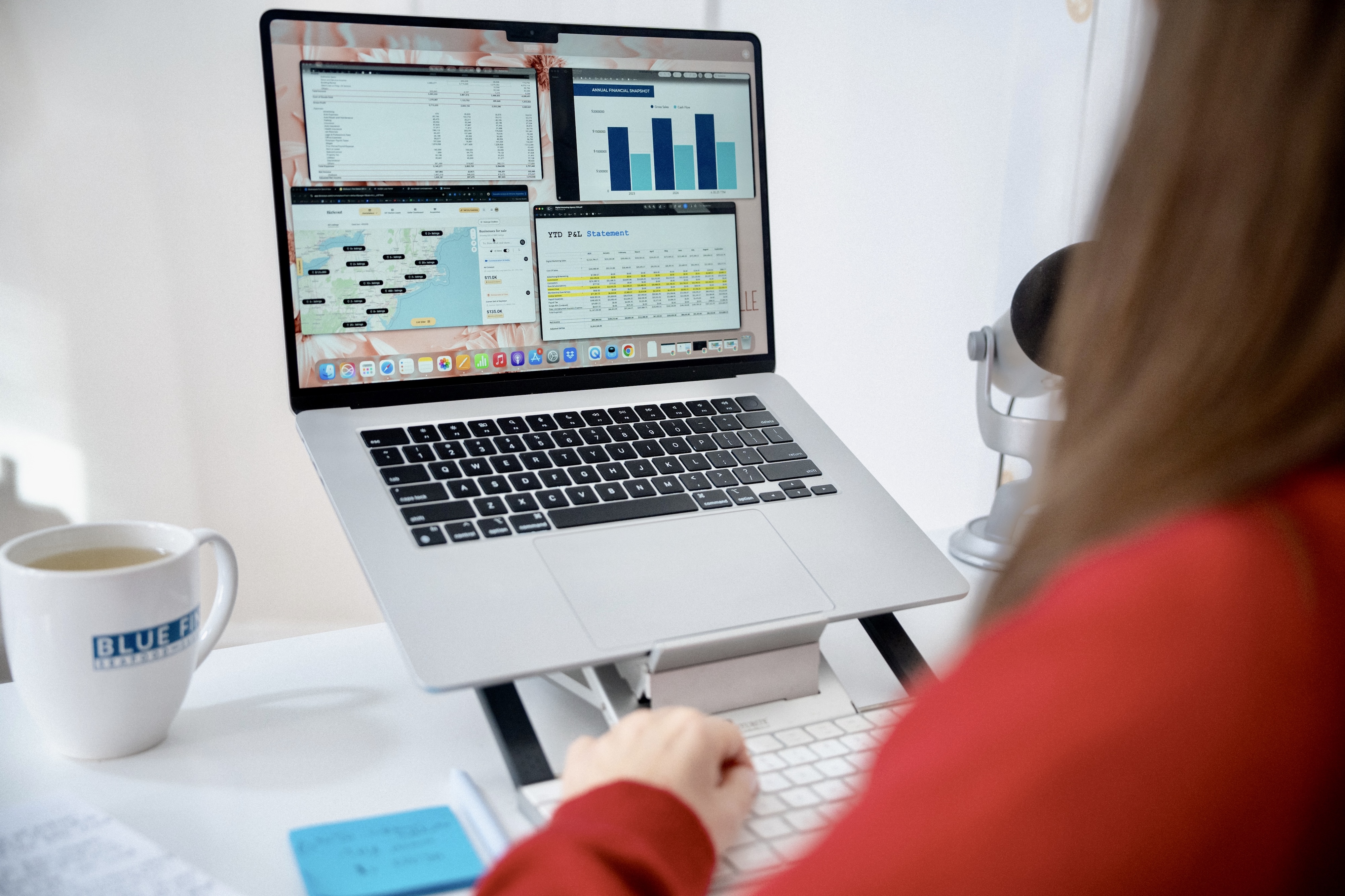 Person working on a laptop displaying financial charts, a map, and a year-to-date P&L statement with a coffee mug labeled Bluefin nearby.