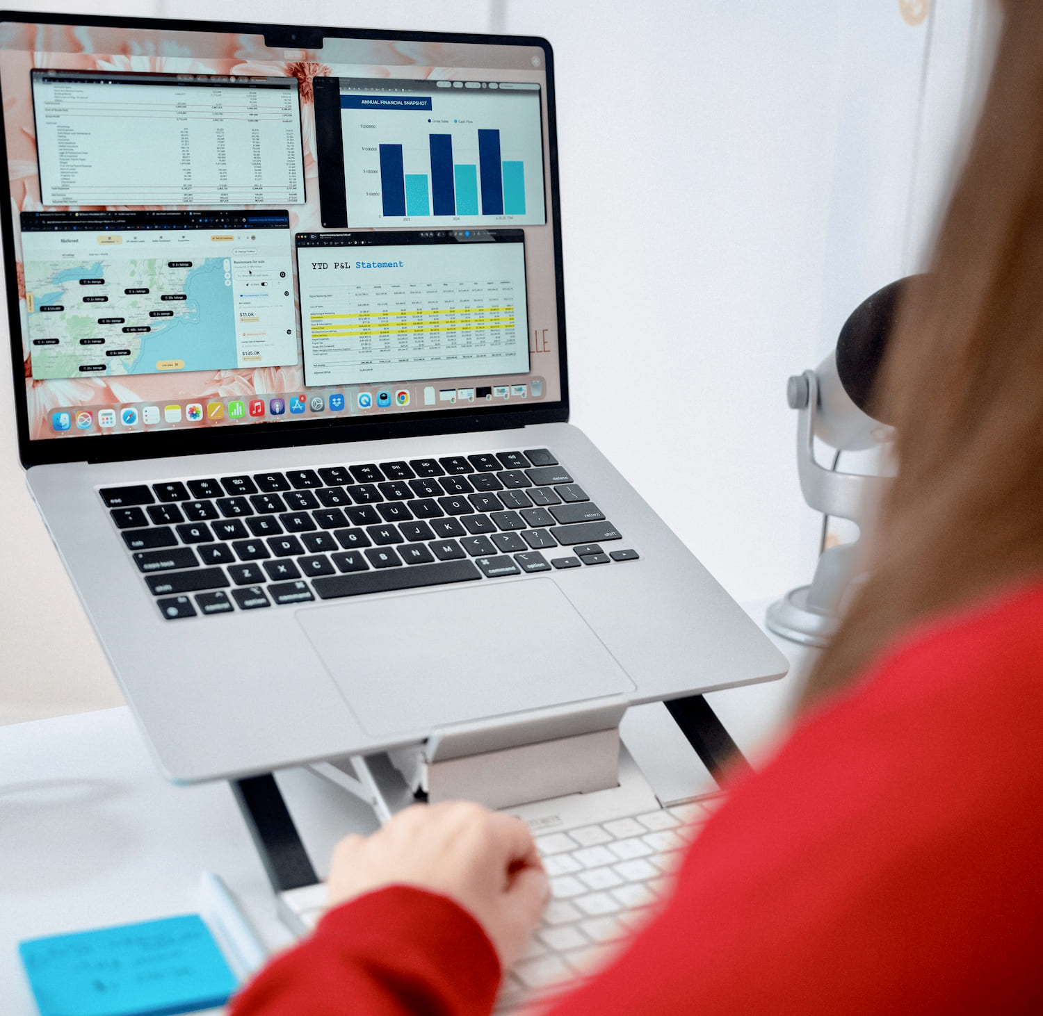 Person in red using a laptop showing financial charts, maps, and a P&L statement on screen.