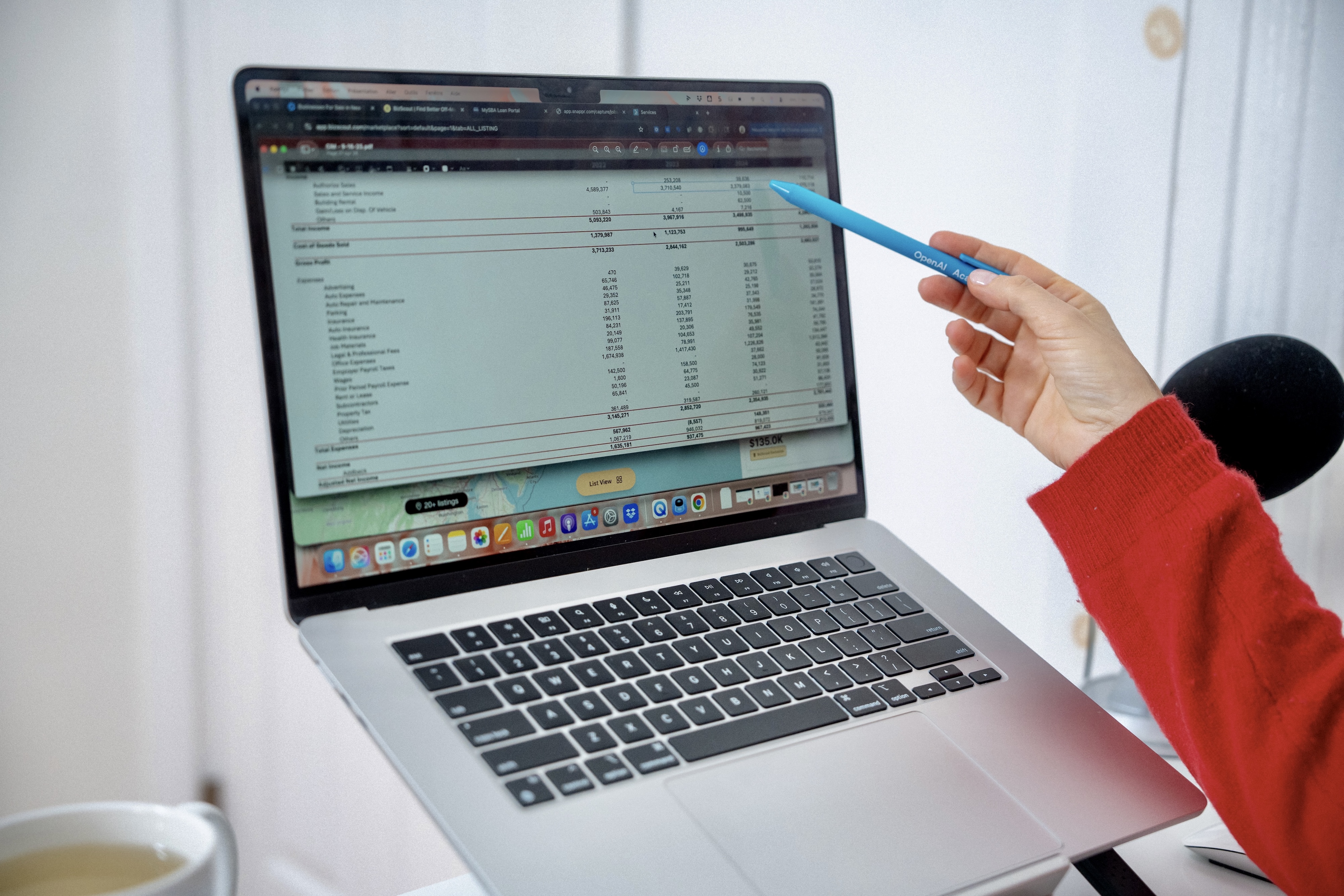 Person in red sweater pointing with a blue pen at financial data on a laptop screen.