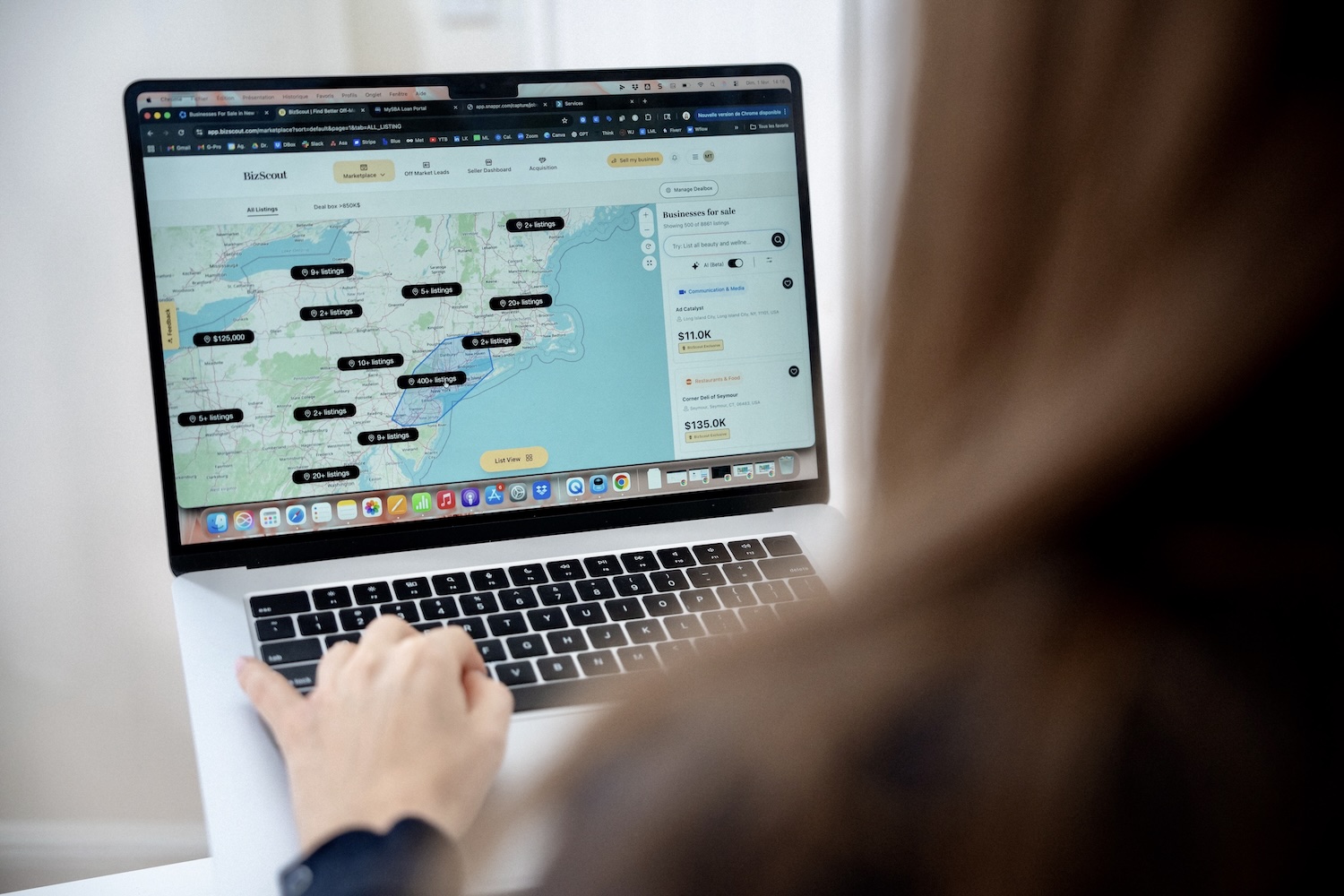 Person using laptop showing a map with business sale listings marked in various locations.