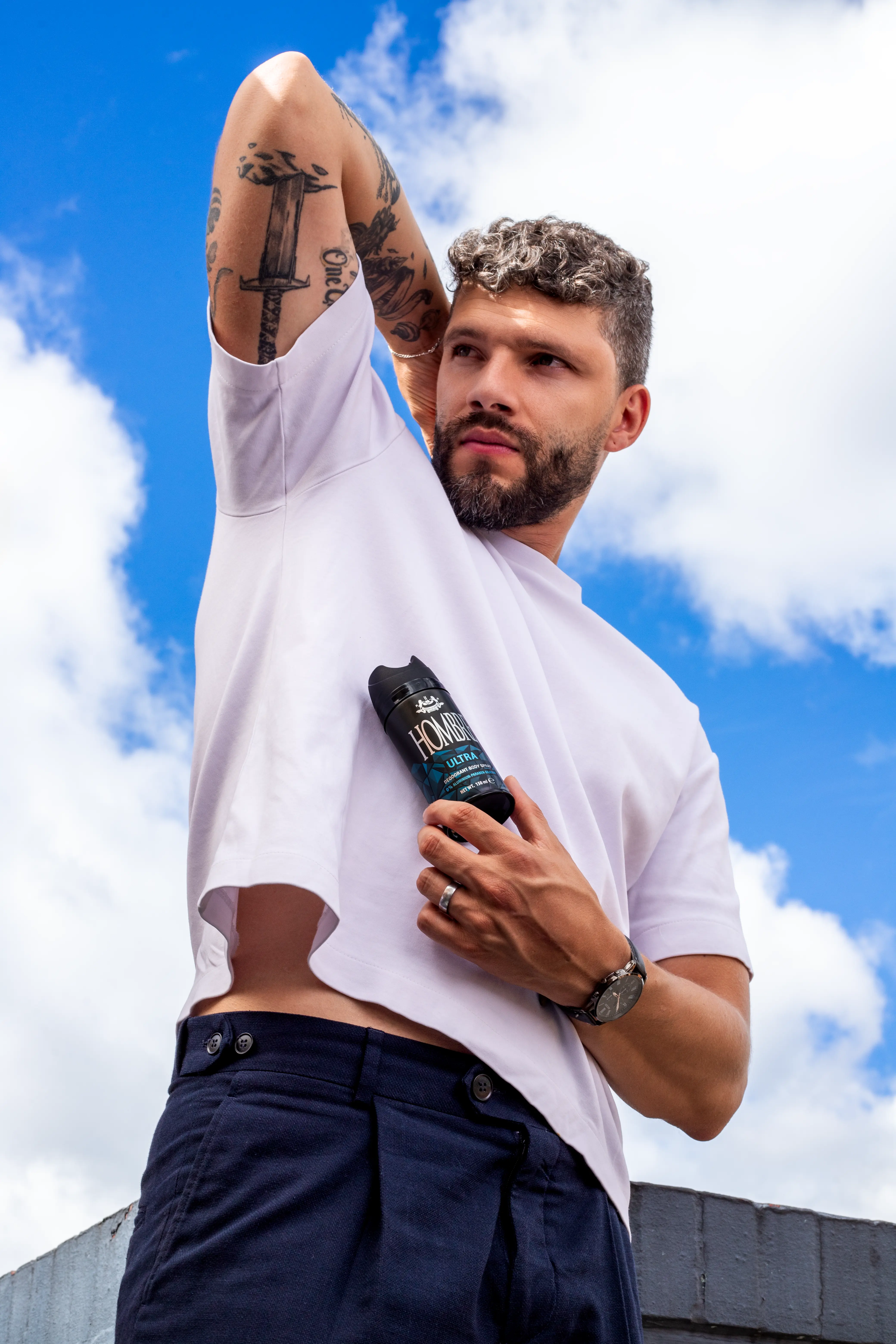 Man holding HOMBRE® Ultra deodorant body spray against blue sky — woody citrus aquatic scent for men