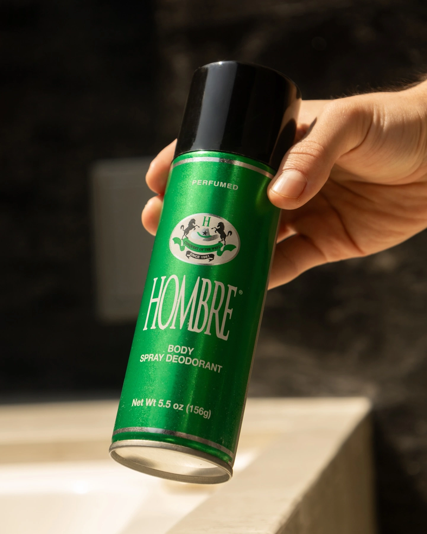 Hand holding HOMBRE® Green deodorant body spray — non-sticky fast-drying formula for men