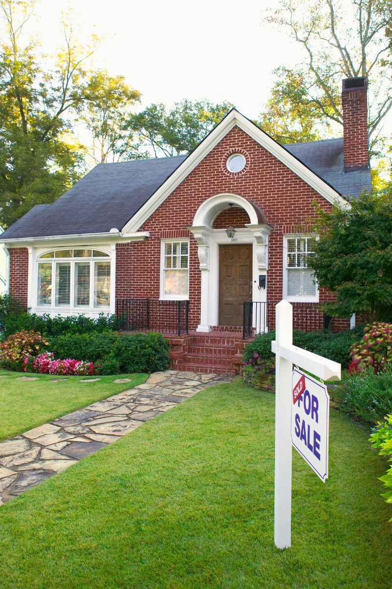 Brick house with a manicured lawn, stone walkway, and a 'Sold' for sale sign in the front yard.