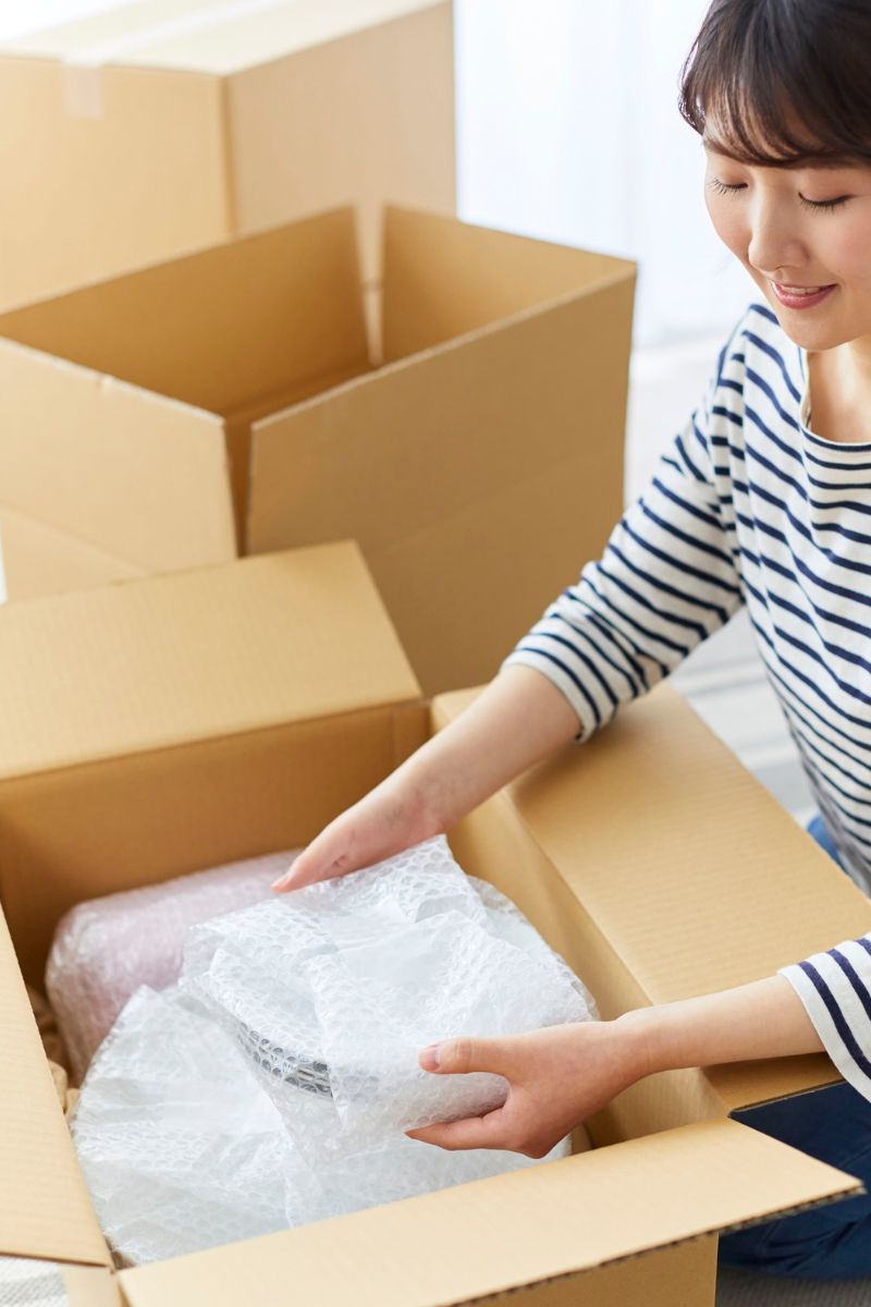Woman unpacking bubble-wrapped items from a cardboard box with additional empty boxes in the background.